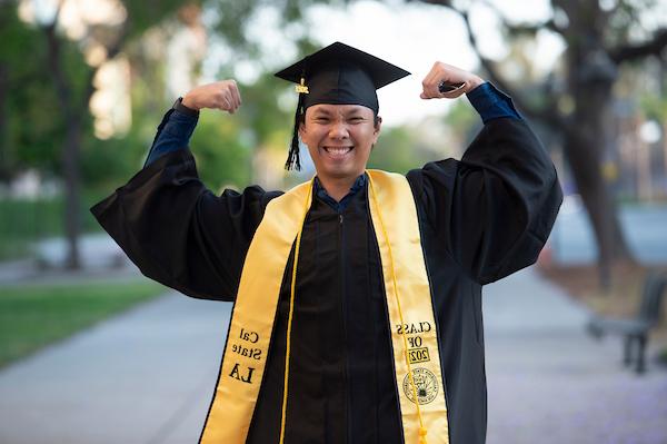 Cal State LA graduate with arms extended wearing black cap and gown.